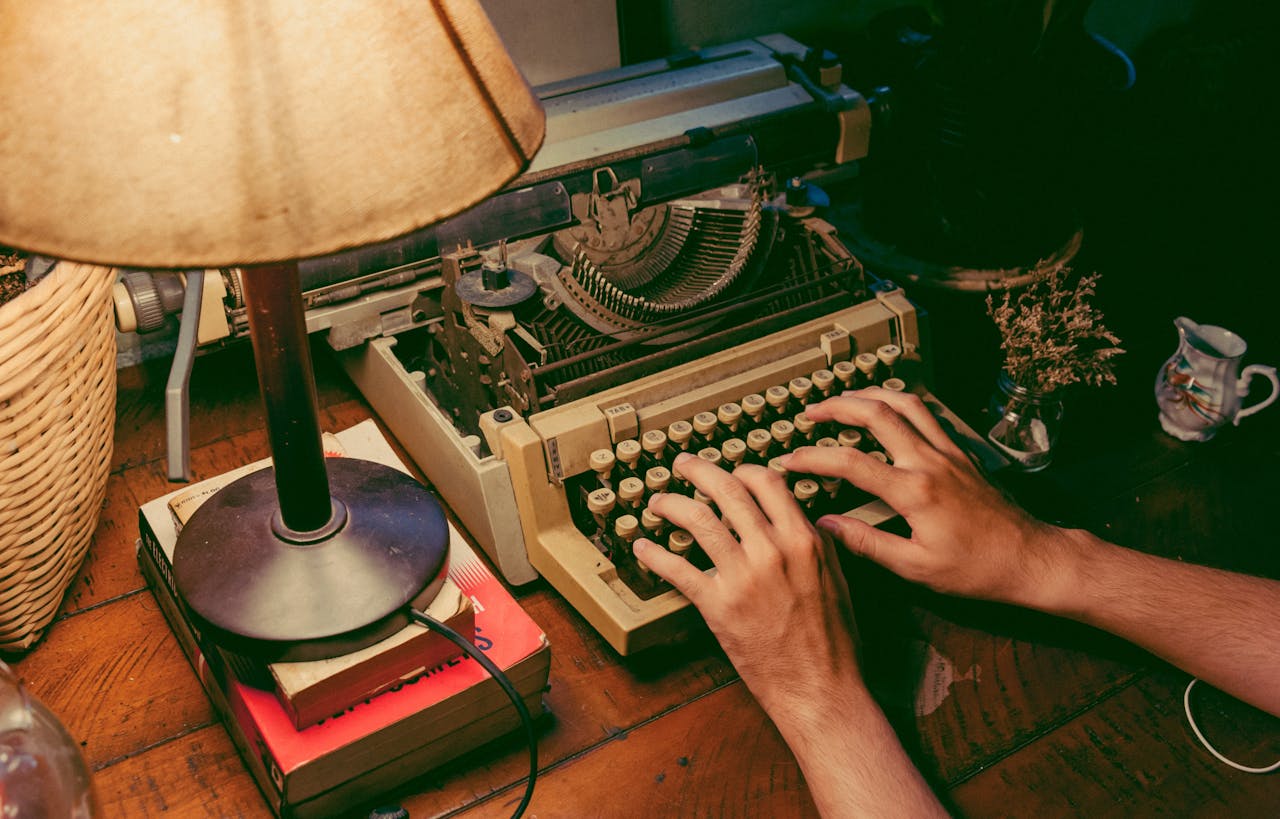 Hands typing on a vintage typewriter under a warm lamp glow, evoking nostalgia.